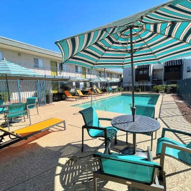 A sunny day at the pool with a striped umbrella providing shade.