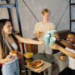 A group of people toasting with blue cups in front of a table with pizza and fries.