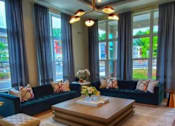 Thumbnail 9 of 17 - A living room with a blue couch, a coffee table, and a vase of flowers.