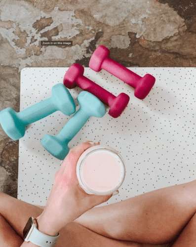 A person is holding a drink and there are two dumbbells on the table.