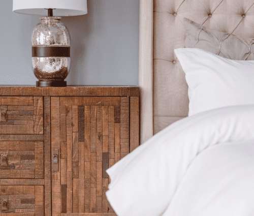 A bedside table with a lamp and a bed with white pillows.