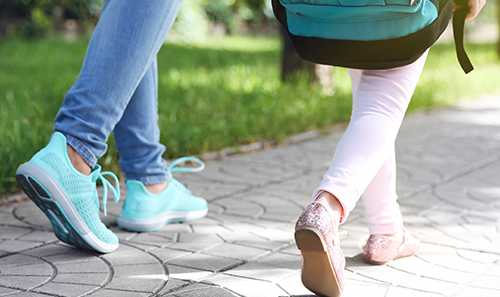 A person in light blue shoes and a teal backpack is walking on a paved path.