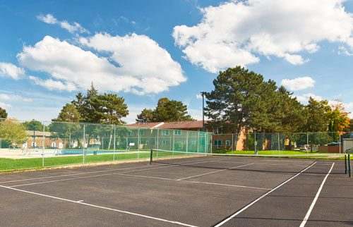Outdoor tennis court in park setting with outdoor pool in the background.