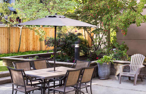 Patio bordered by green grass, with various patio furniture on the large concrete tiles.