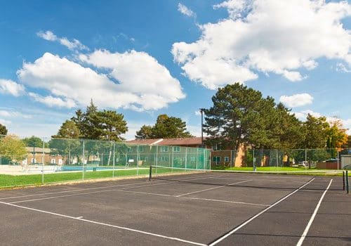 Outdoor tennis court in park setting with outdoor pool in the background.