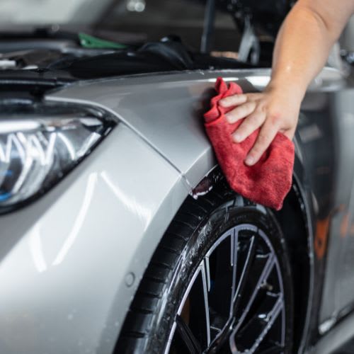 A person is cleaning a car with a red cloth.