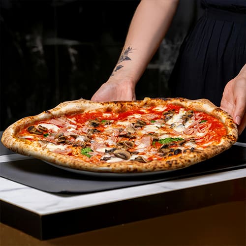 A person holding a pizza with various toppings.
