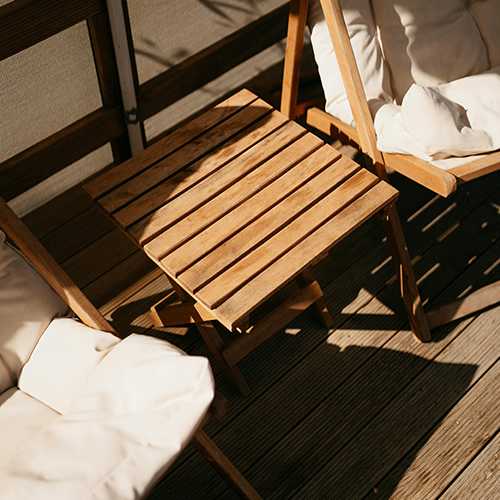 A wooden chair and table are on a wooden deck.