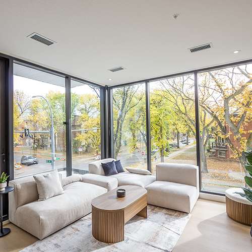 A modern living room with a large window overlooking a tree-lined street.