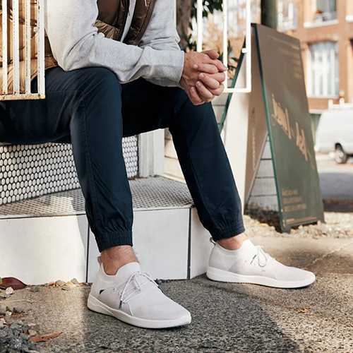 A person is sitting on a white bench wearing white sneakers and dark pants.