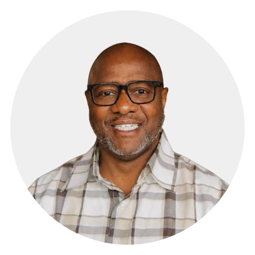 A man with glasses and a beige blazer over a white shirt.