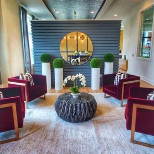 A room with a round mirror, a table with a vase of flowers, and chairs with red cushions.