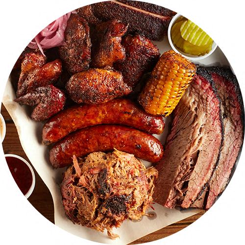 A plate of barbecued meats including sausages, ribs, and pulled pork.