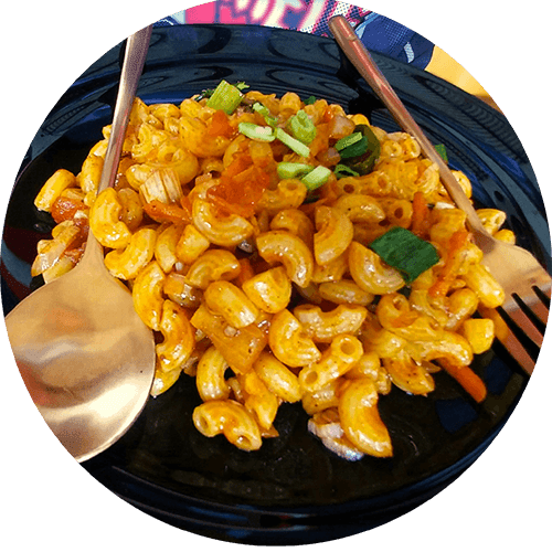 A black plate filled with macaroni and cheese topped with green onions.