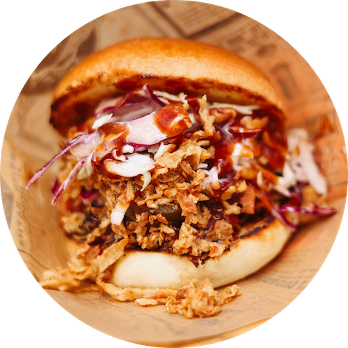 a pulled pork sandwich with coleslaw on a wooden plate