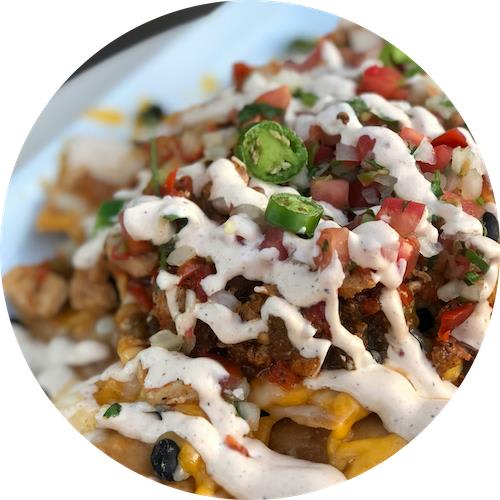 A plate of nachos topped with cheese, jalapeños, and a white sauce.