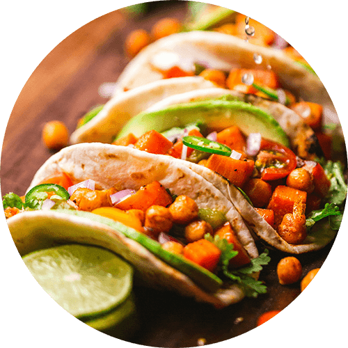 Three tacos with vegetables and chickpeas on a wooden surface.