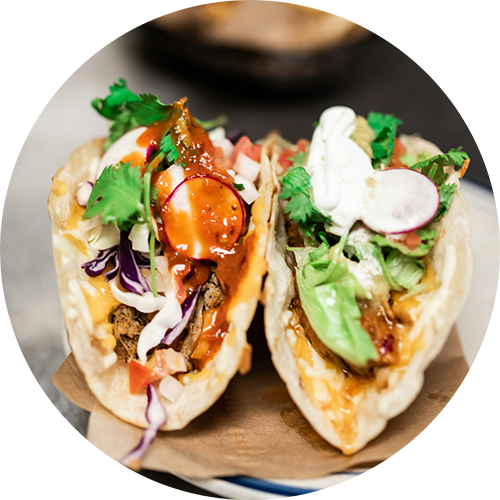 Two tacos with meat, lettuce, and radishes on a wooden board.