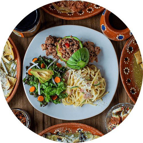 A plate of spaghetti with meat and vegetables is surrounded by various dishes.