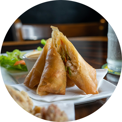 A plate of fried spring rolls with a side of dipping sauce.