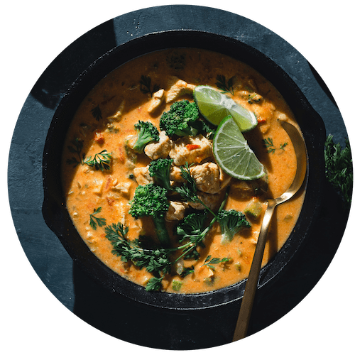 a bowl of thai red curry with chicken and broccoli in a black bowl with a spoon