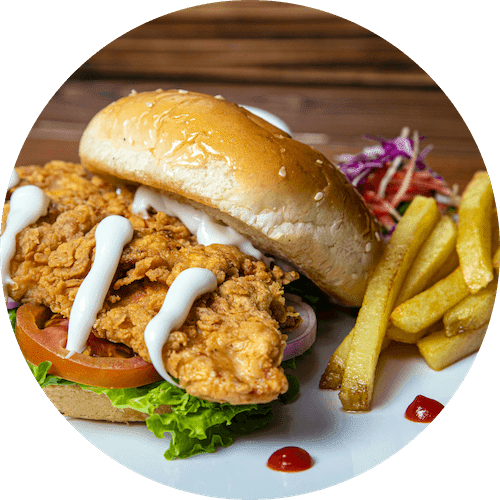 A sandwich with fried chicken, lettuce, tomato, and onion on a bun with fries and coleslaw on the side.