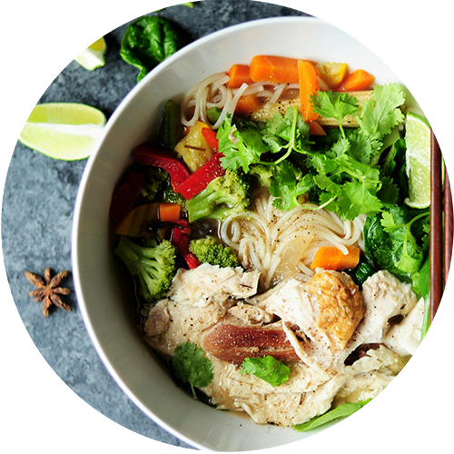 A bowl of noodles with chicken, vegetables, and herbs.