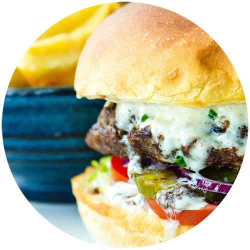 a cheeseburger on a bun with a blue bowl of fries