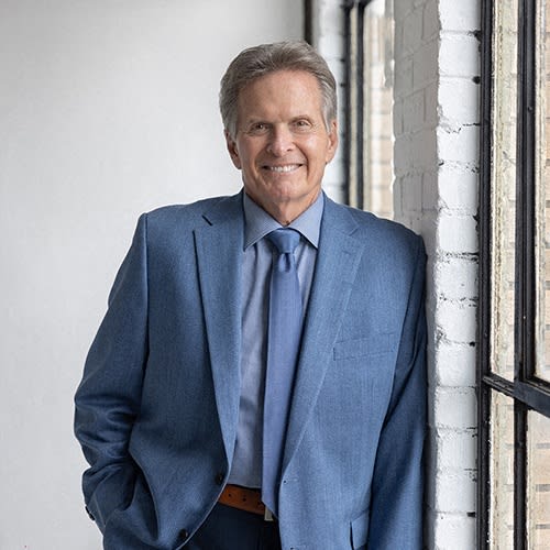 a man in a blue suit and tie leaning against a window