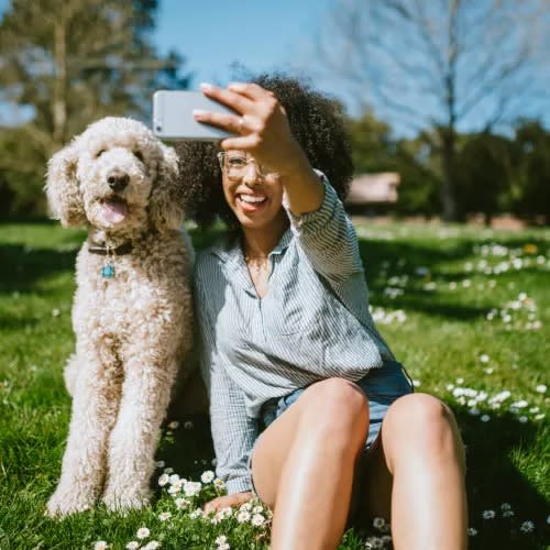 a woman sitting in the grass with her dog and taking a picture with her phone at Cabana Club Apartments in Jacksonville, Florida