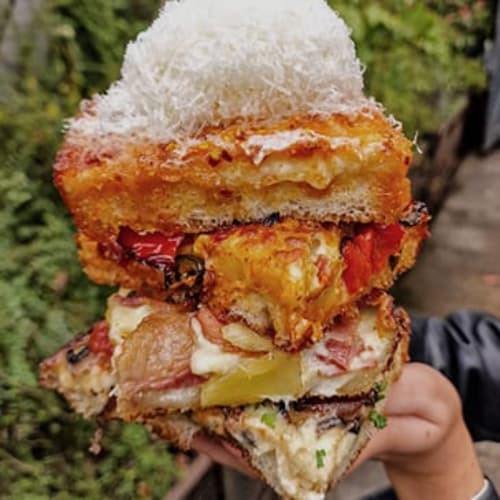 A person is holding a sandwich with a toasted bun, cheese, and tomato.