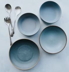 a set of four blue and copper metal plates and spoons on a white background
