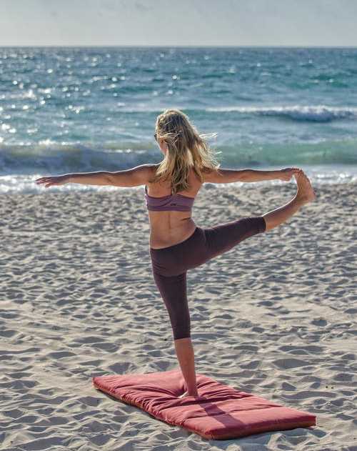 A woman is practicing yoga on a red mat at the beach at Pembroke Pines Landings, Pembroke Pines