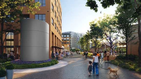 A modern building with a cylindrical structure in the foreground and people walking a dog on a path.