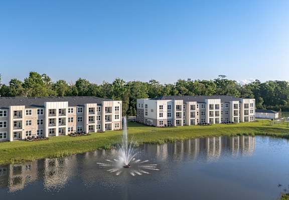A fountain in the middle of a pond in front of a building.