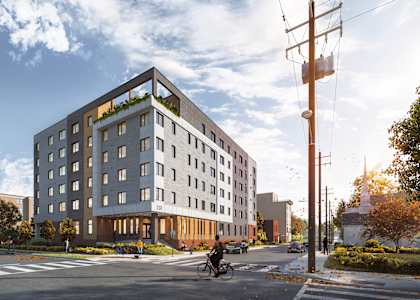 A modern building with a green roof is situated on a street corner with a cyclist passing by.