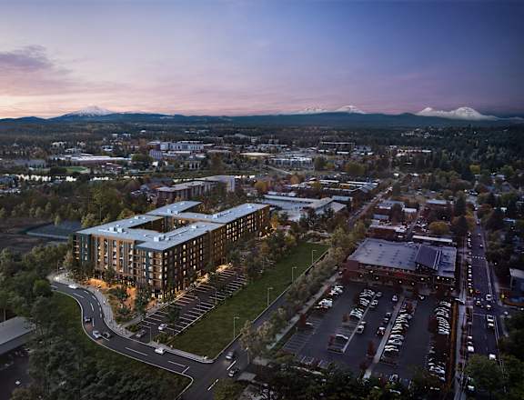 A modern building with a curved glass facade is the focal point of a bustling cityscape at dusk.