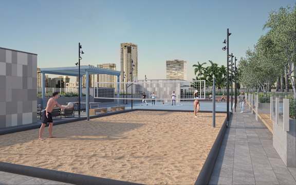 A man is playing beach volleyball in a sandy area with a city skyline in the background.