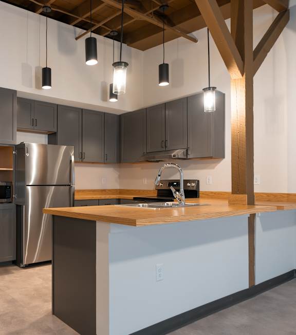 A modern kitchen with a wooden ceiling beam and pendant lights.