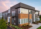 Thumbnail 2 of 22 - A modern two-story apartment building with balconies and a well-maintained lawn in front.