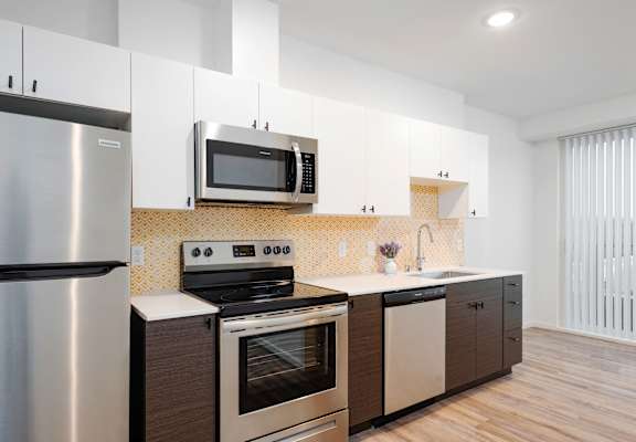 A modern kitchen with a stainless steel refrigerator, microwave, oven, and wooden cabinets at Green Lake Apartments in Seattle, The Loop.