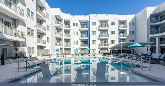 A large pool surrounded by apartment buildings with a blue sky in the background.