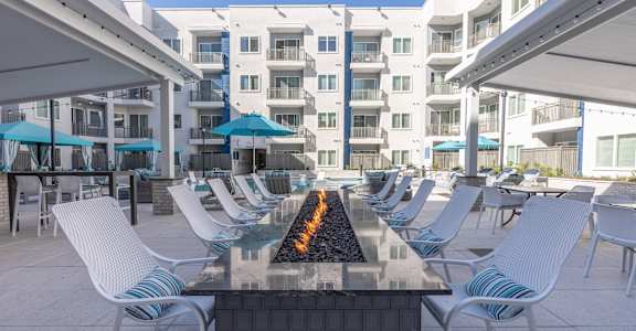 A patio with white chairs and a fire pit in the middle.