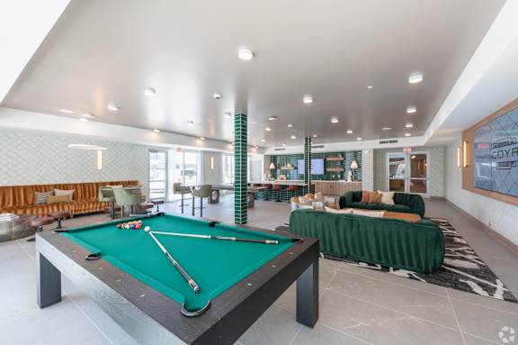 A pool table is in the middle of a room with a green couch.