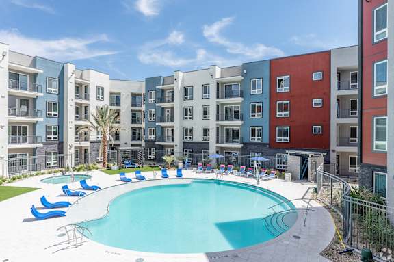 A swimming pool surrounded by a fence and chairs in front of apartment buildings.