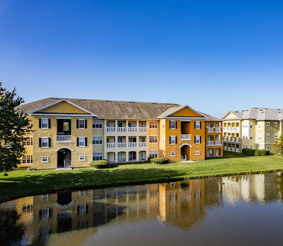 A large building with a yellow facade is reflected in the water in front of it.