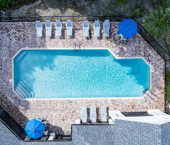 A rectangular pool surrounded by a brick patio and lounge chairs.