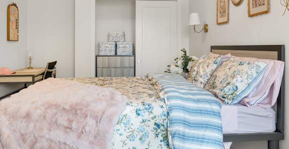 A bed with a pink comforter and a blue striped pillow is in the foreground.