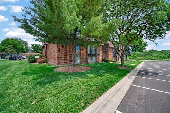 A parking lot is in front of a building with a green lawn and trees.