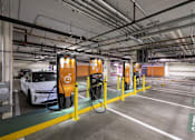 Thumbnail 12 of 13 - A white car is refueling at a yellow pump in a parking garage.